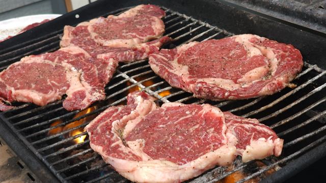 Seasoned ribeye steaks on an open-fire grill