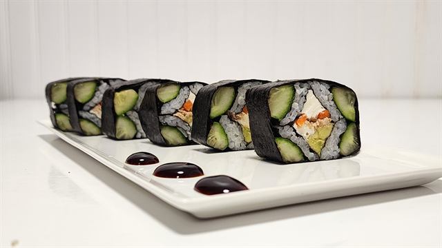 Cucumber-wrapped sushi rolls plated with dots of sauce