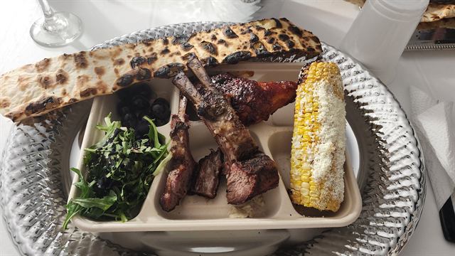 Plate of grilled meats, corn on the cob, greens, and flatbread