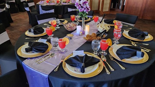 Round table with gold chargers, black napkins, flowers, and fruit drinks