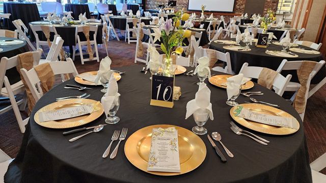 Banquet table with gold chargers, printed menus, and a floral centerpiece