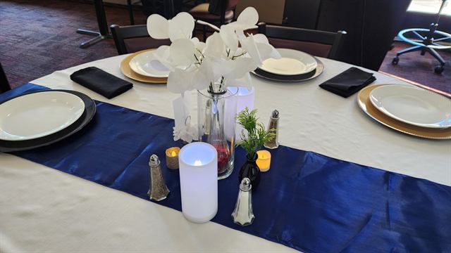 White table with a navy runner, gold chargers, and a white orchid centerpiece