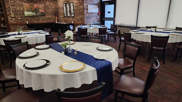 Dining room of round tables set with gold chargers and navy runners